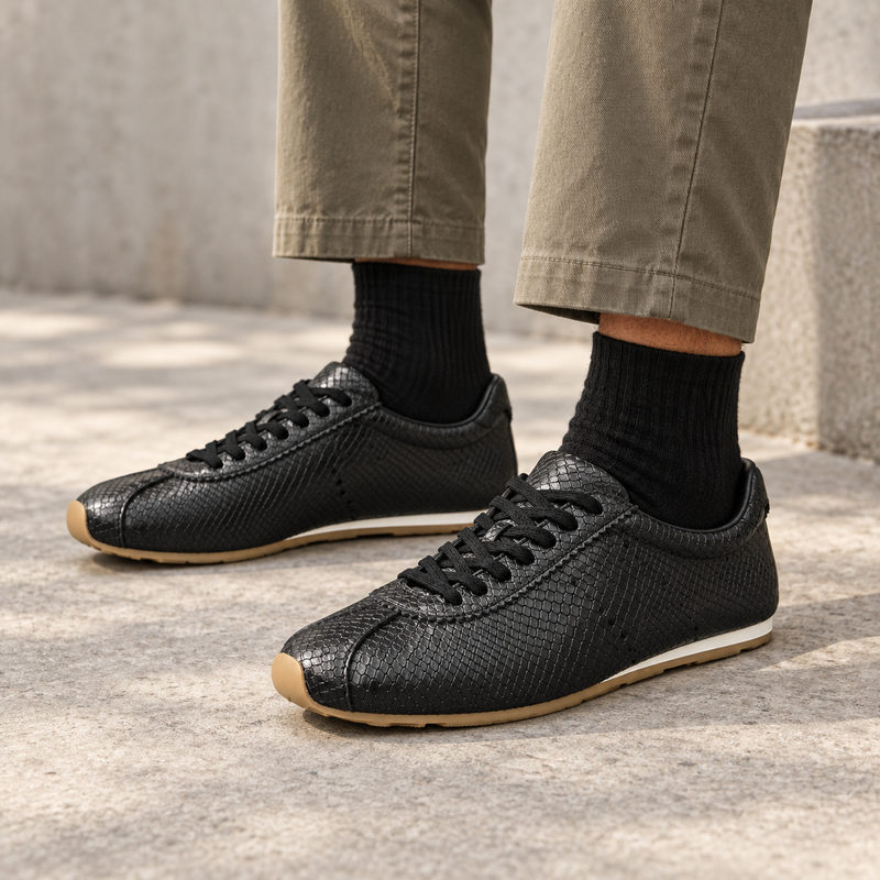Black snake-embossed lace-up sneakers worn with khaki trousers and black ribbed socks