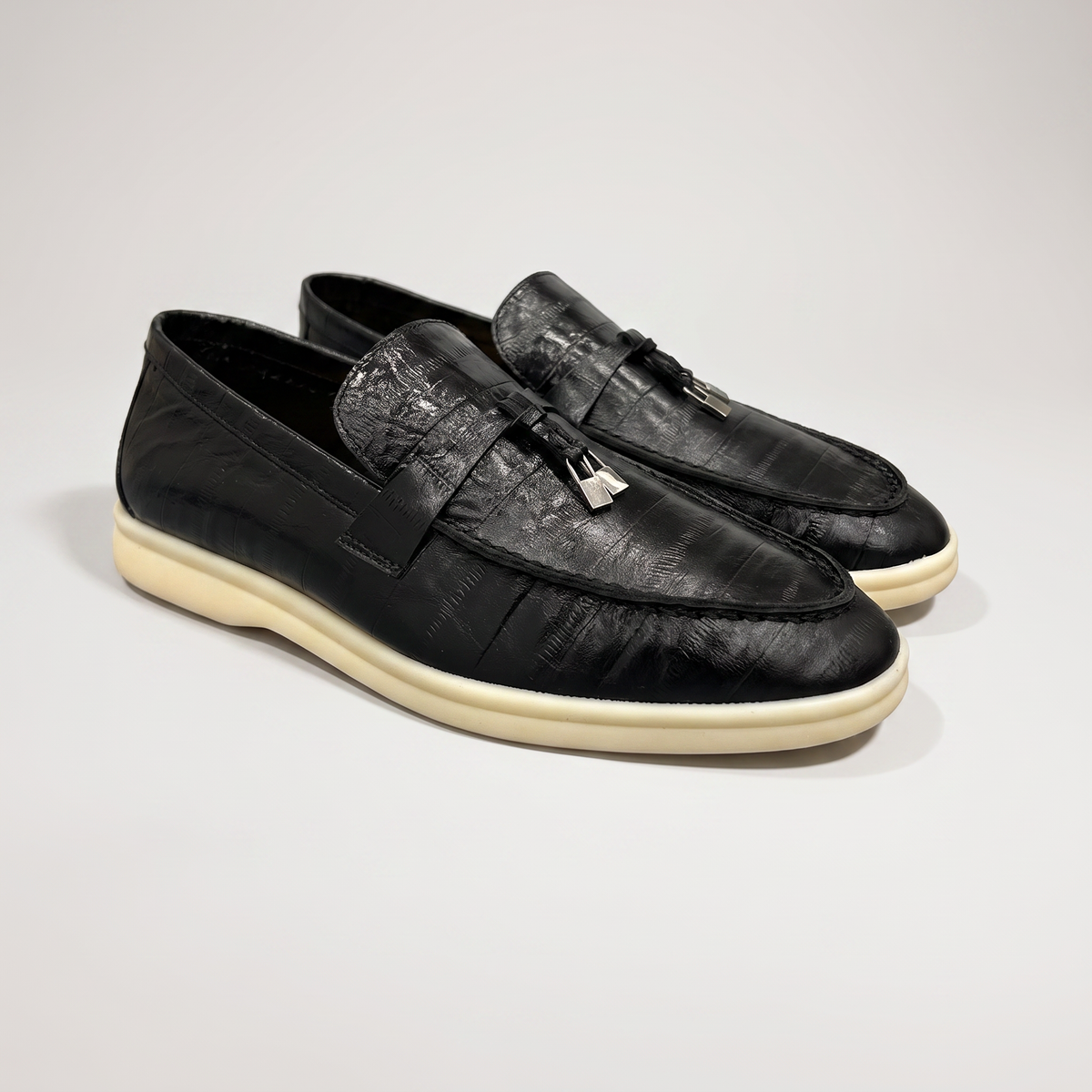 Black loafer pair three-quarter view showing an eel-pattern embossed vamp and tassel detail