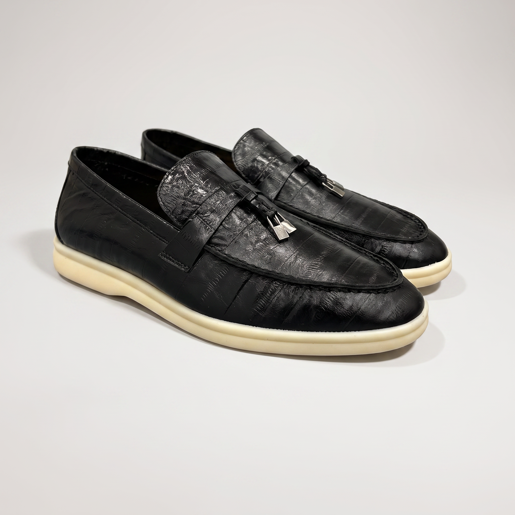Black loafer pair three-quarter view showing an eel-pattern embossed vamp and tassel detail