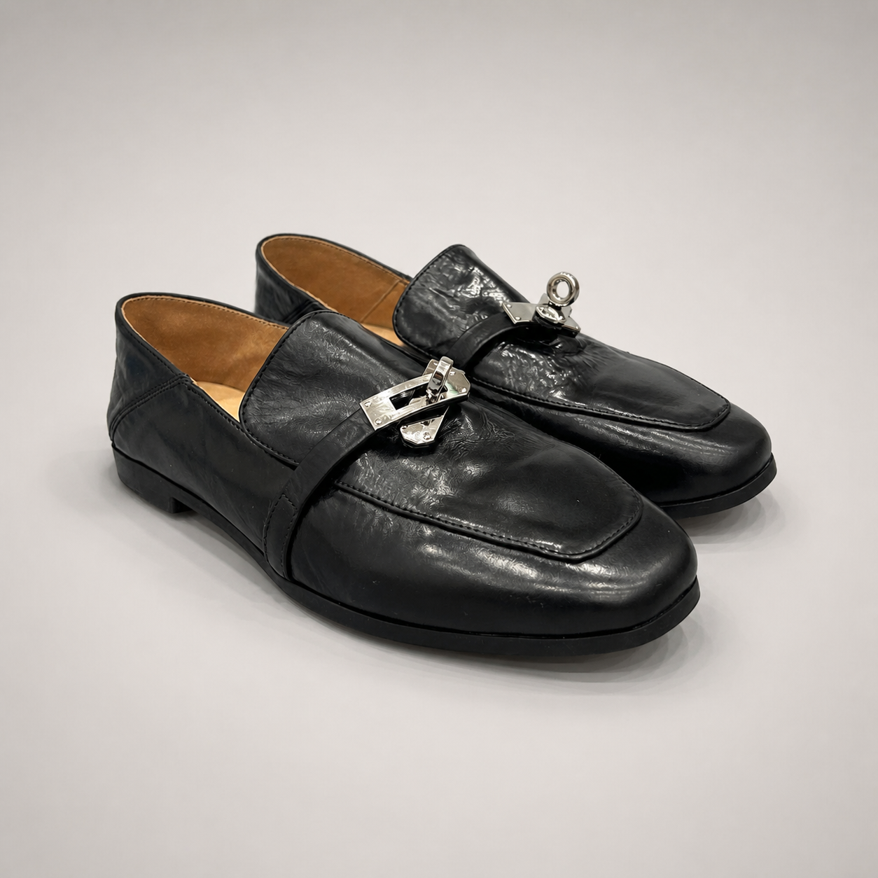 Black loafer pair three-quarter view showing a metal accent across the vamp