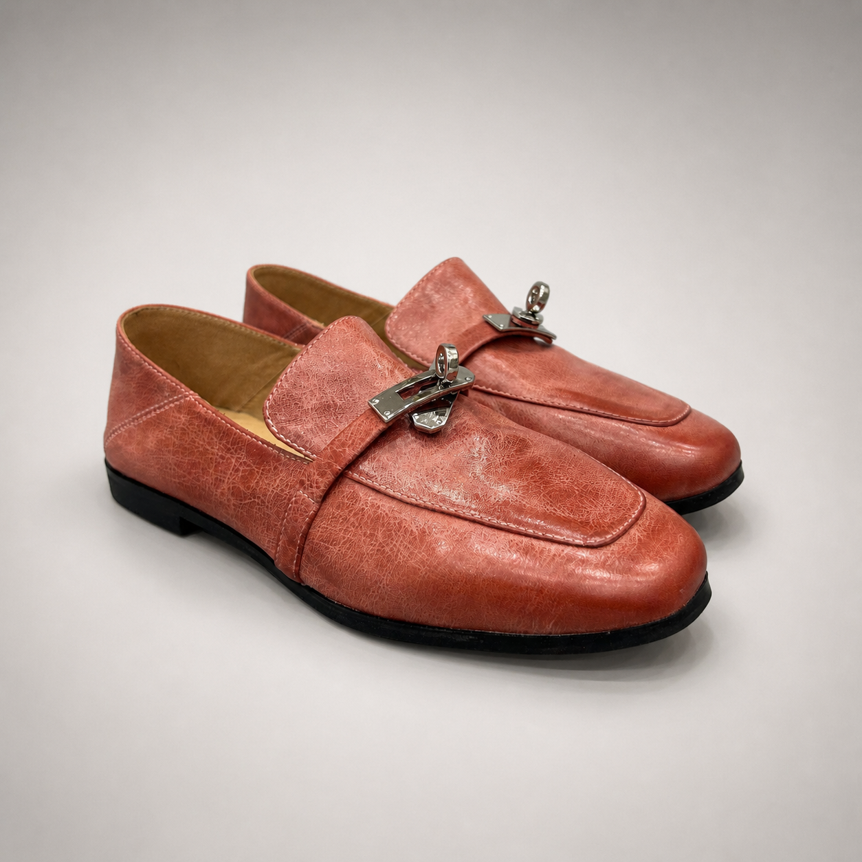 Rust loafer pair three-quarter view showing a metal accent across the vamp