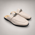 Ivory mule loafer pair three-quarter view showing an open-back mule construction and metal vamp accent