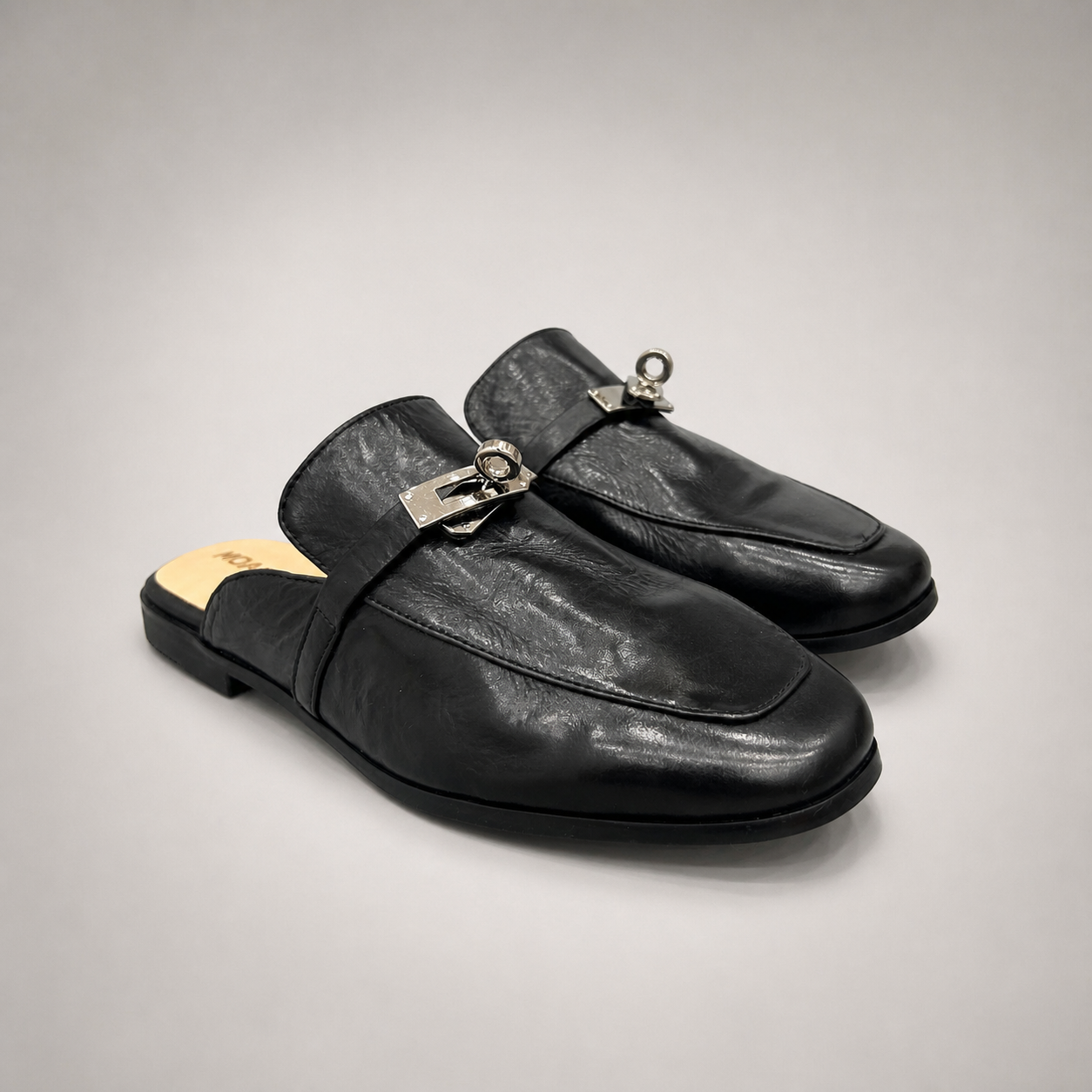Black mule loafer pair three-quarter view showing an open-back mule construction and metal vamp accent