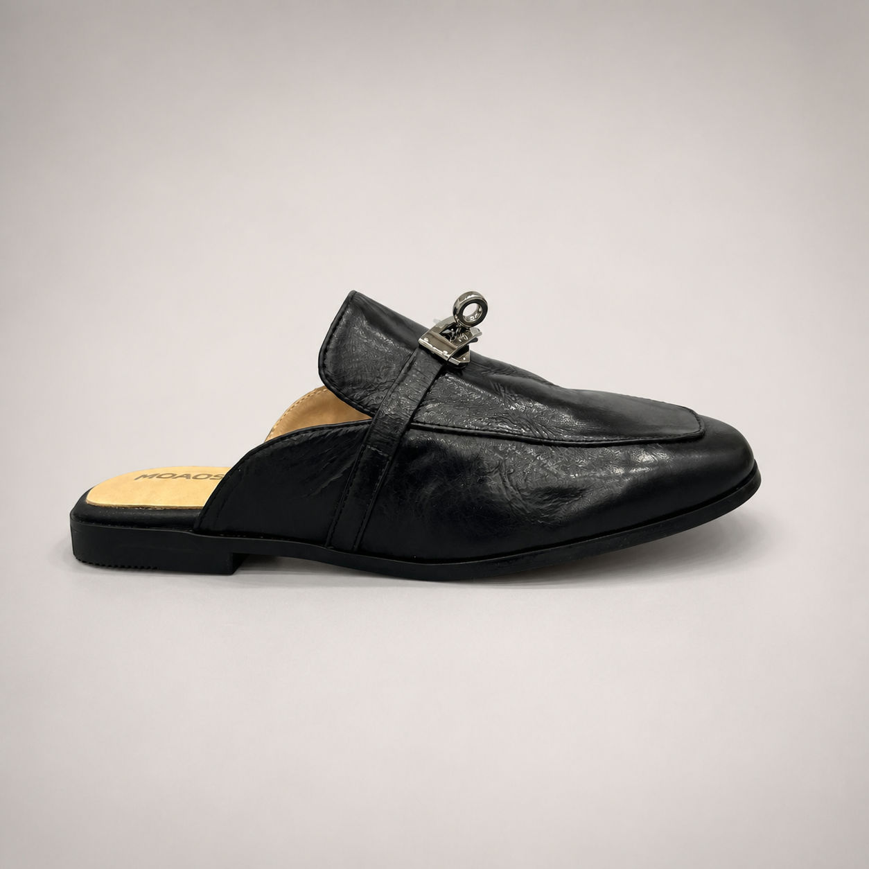 Black mule loafer side profile showing an open-back mule construction and metal vamp accent