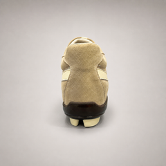 Beige soccer shoe rear view showing a lace-up upper and molded outsole studs