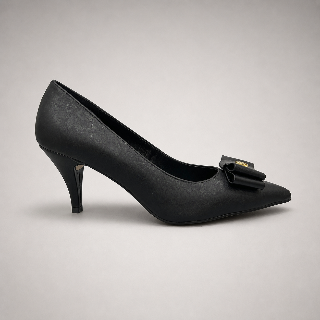 Black pump side profile showing a pointed toe and bow-shaped vamp ornament