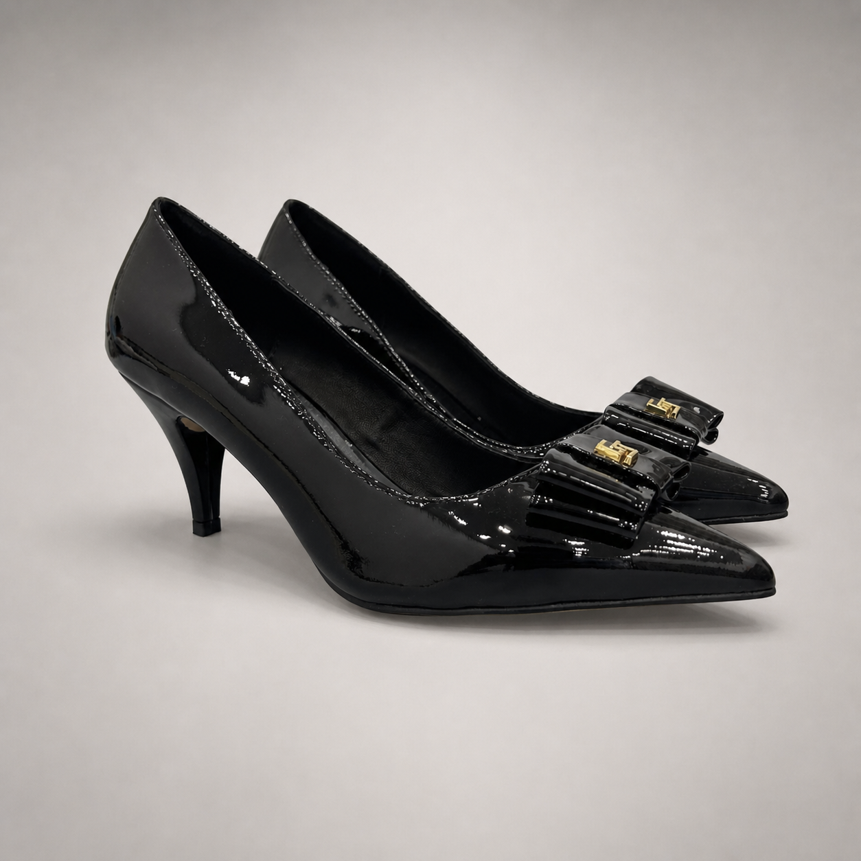 Black pump pair three-quarter view showing a pointed toe and bow-shaped vamp ornament