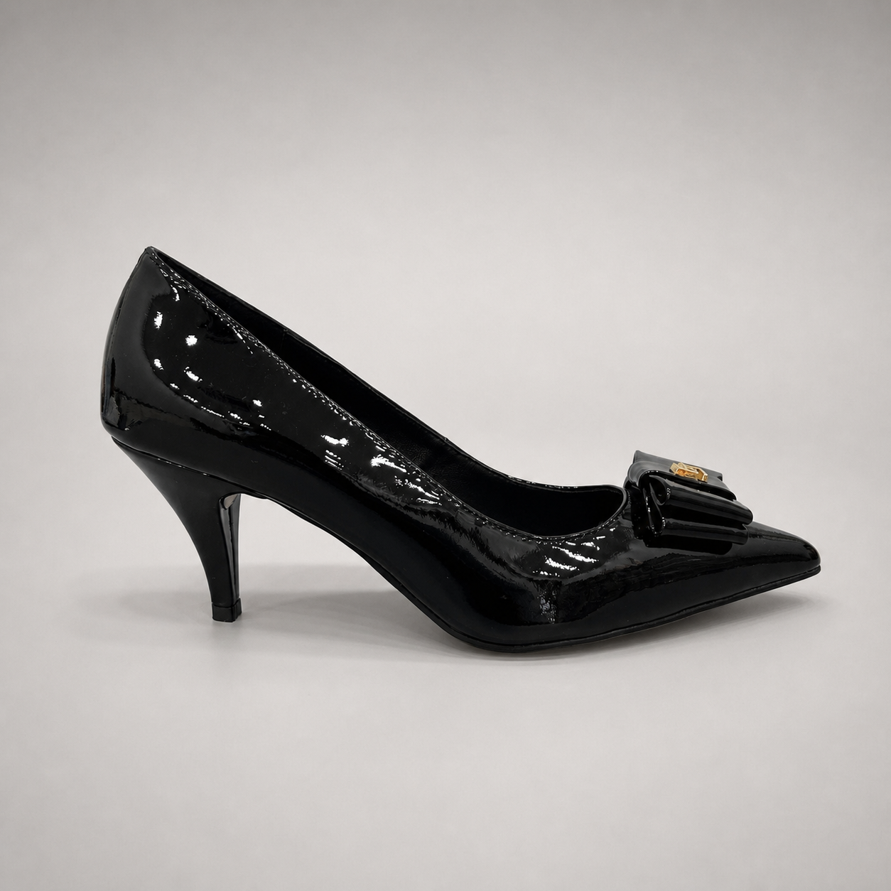 Black pump side profile showing a pointed toe and bow-shaped vamp ornament