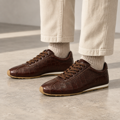 Dark brown croc-embossed oil-waxed leather low-profile sneakers worn with ivory trousers and oatmeal socks