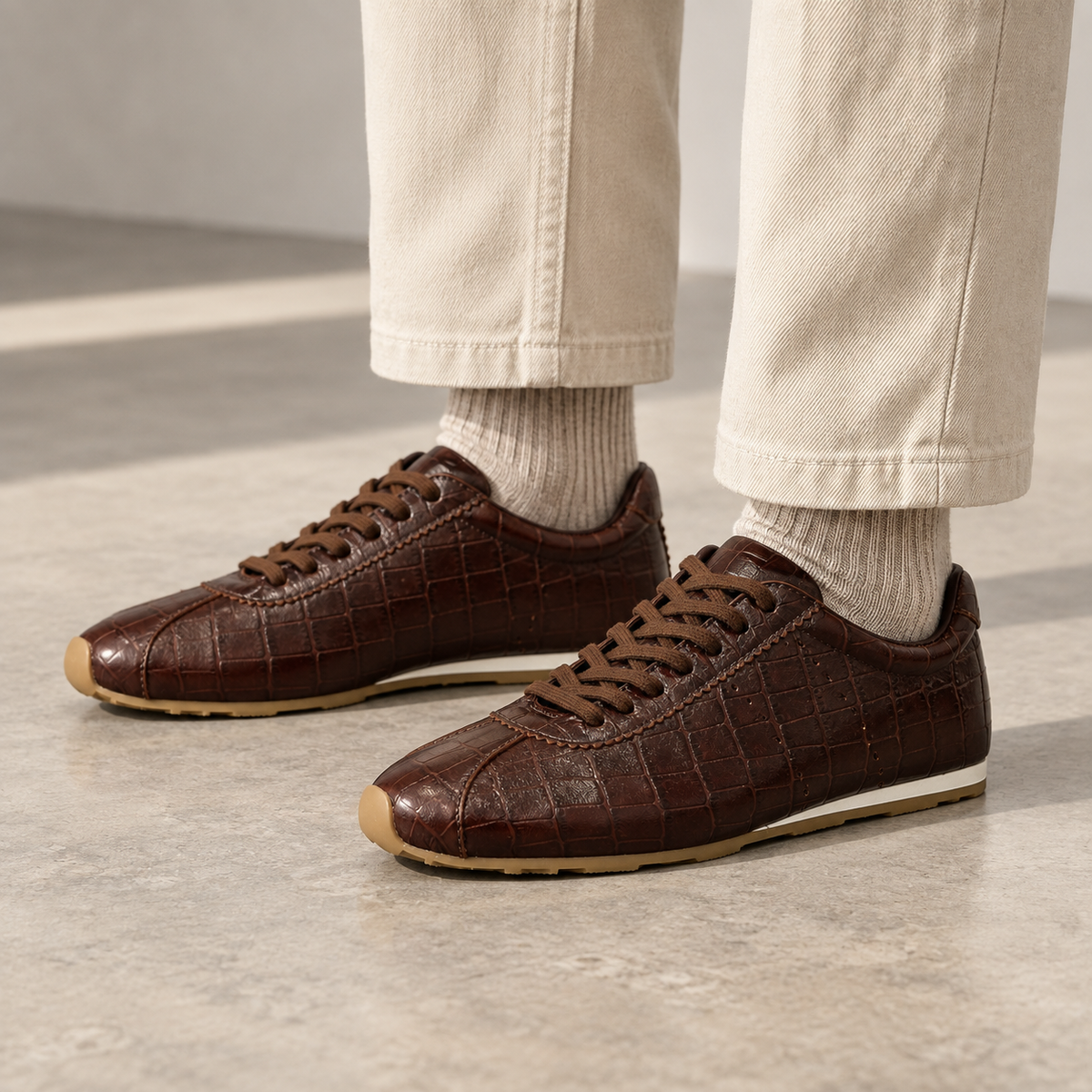 Dark brown croc-embossed oil-waxed leather low-profile sneakers worn with ivory trousers and oatmeal socks