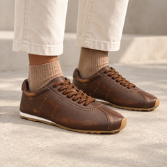 Brown smooth oil-waxed leather low-profile sneakers worn with cream trousers and tan socks