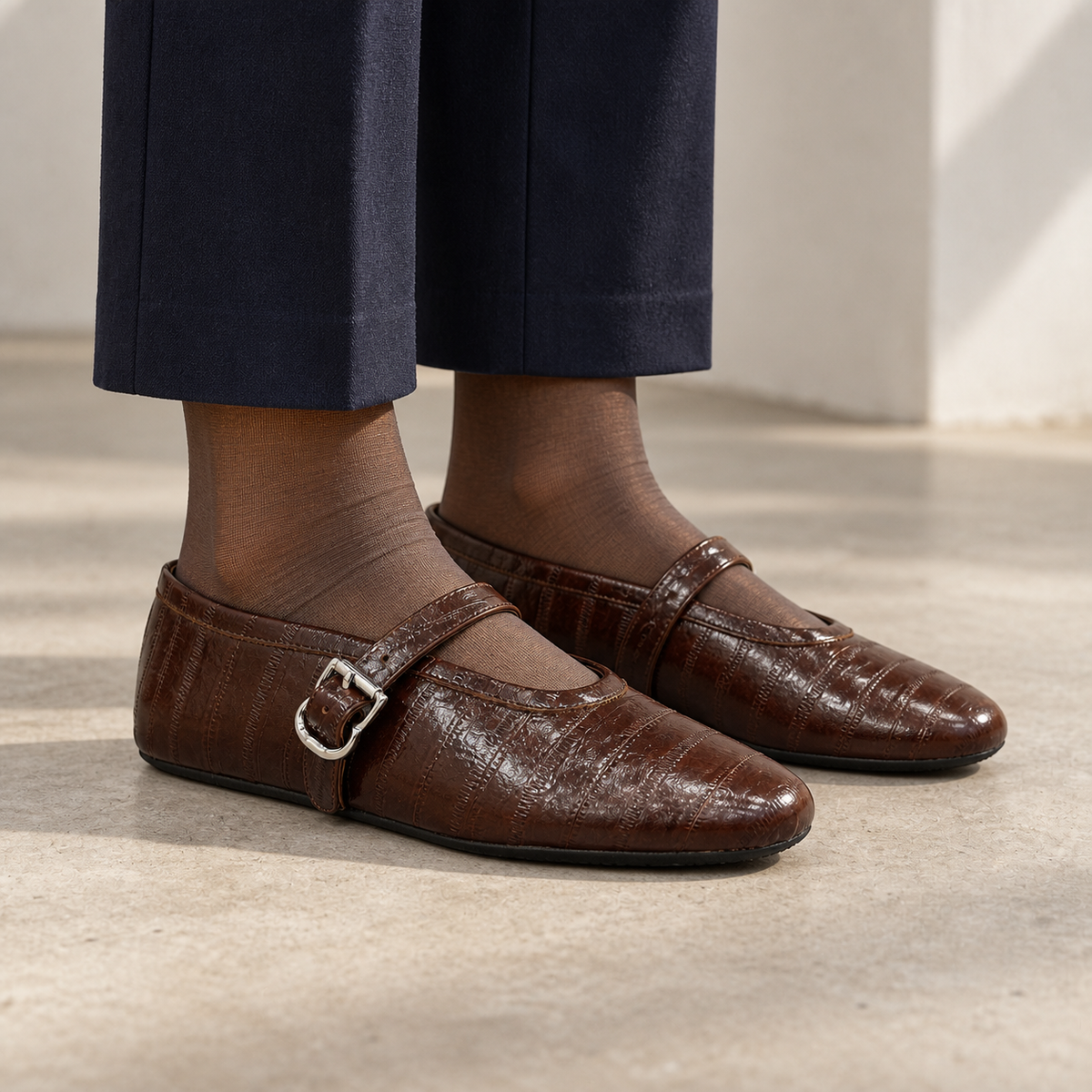 Dark brown eel-embossed oil-waxed leather buckle-strap flats worn with navy trousers and sheer taupe socks