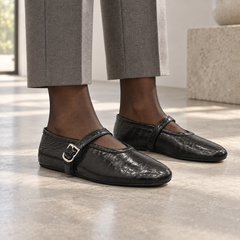 Black eel-embossed oil-waxed leather buckle-strap flats worn with grey tailored trousers and sheer hosiery