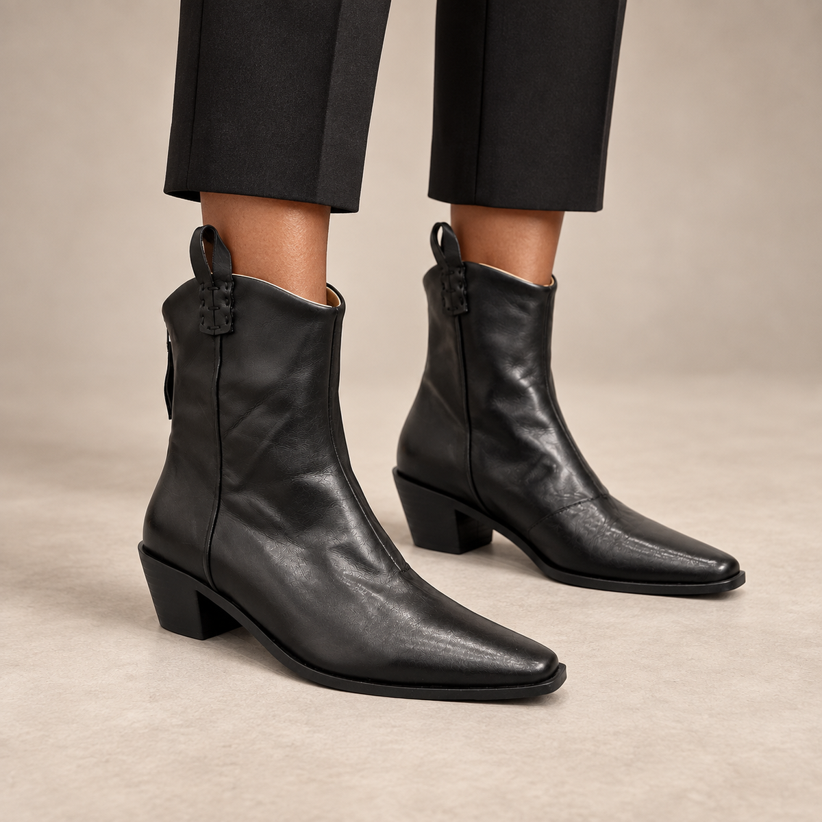 Black pointed-toe leather ankle boots worn with cropped black trousers
