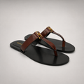 Brown flat sandal pair three-quarter view showing a flat sole with a toe-loop strap
