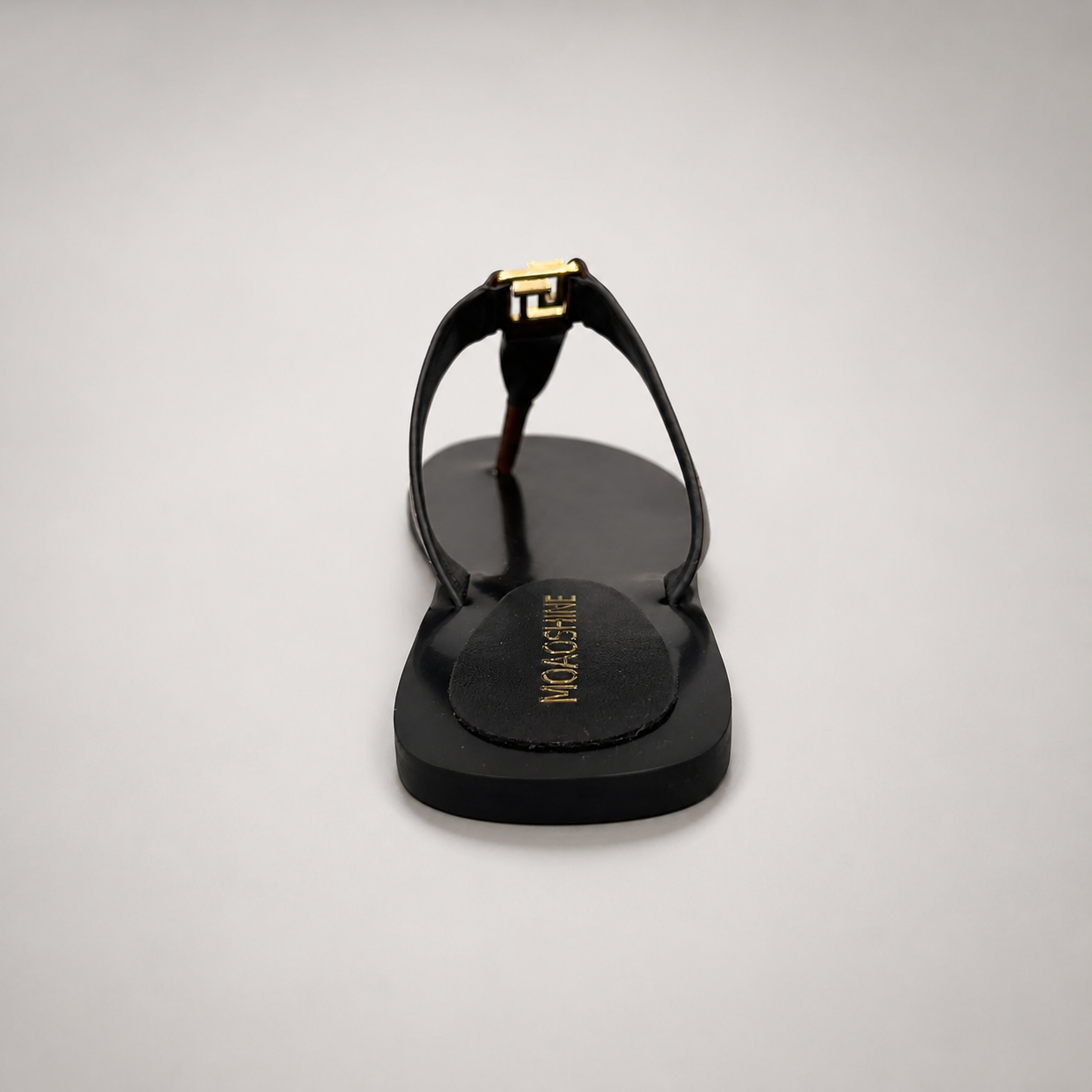 Brown flat sandal rear view showing a flat sole with a toe-loop strap