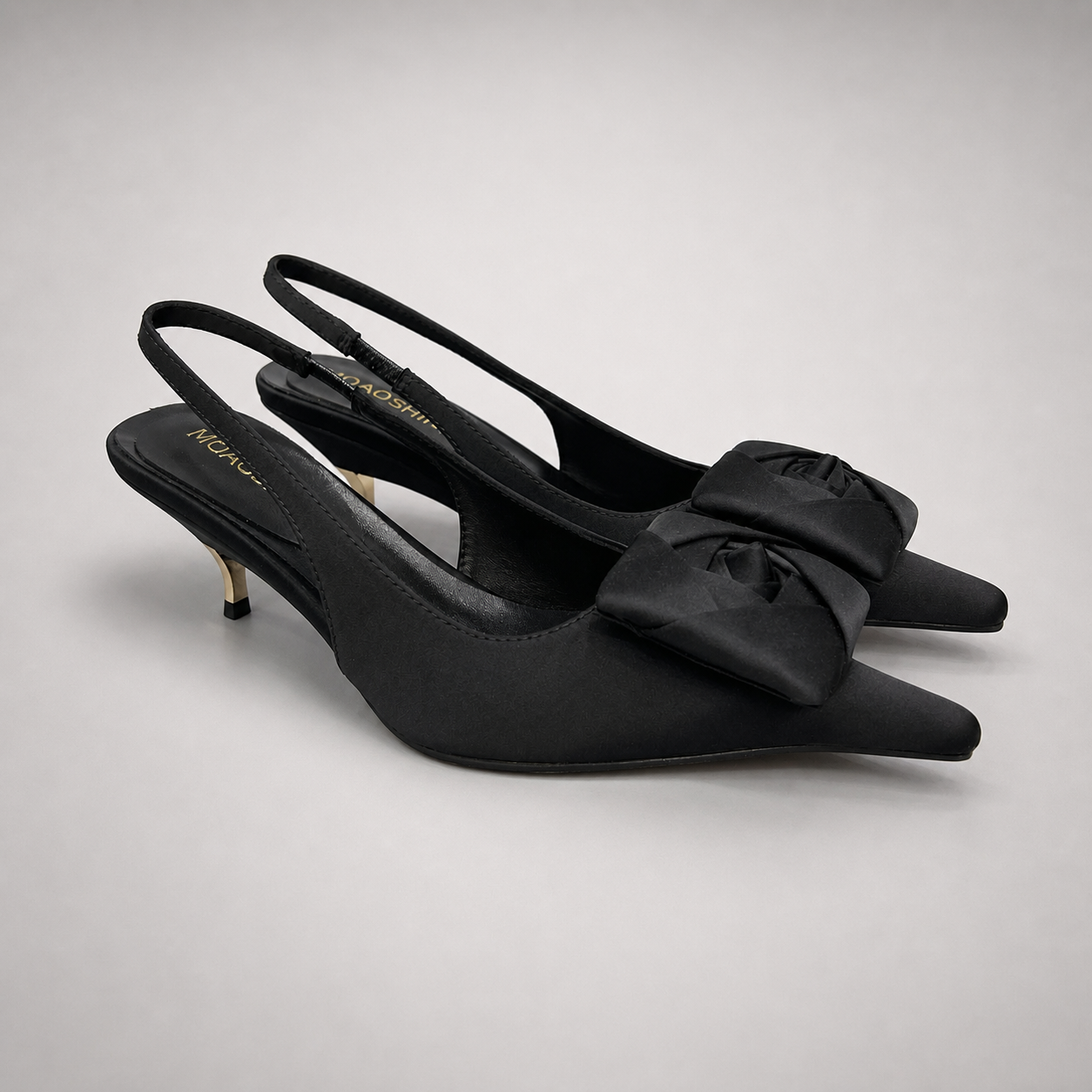 Black slingback pump pair three-quarter view showing a pointed toe and bow detail