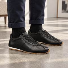 Black eel-embossed oil-waxed leather low-profile sneakers worn with navy trousers and black ribbed socks