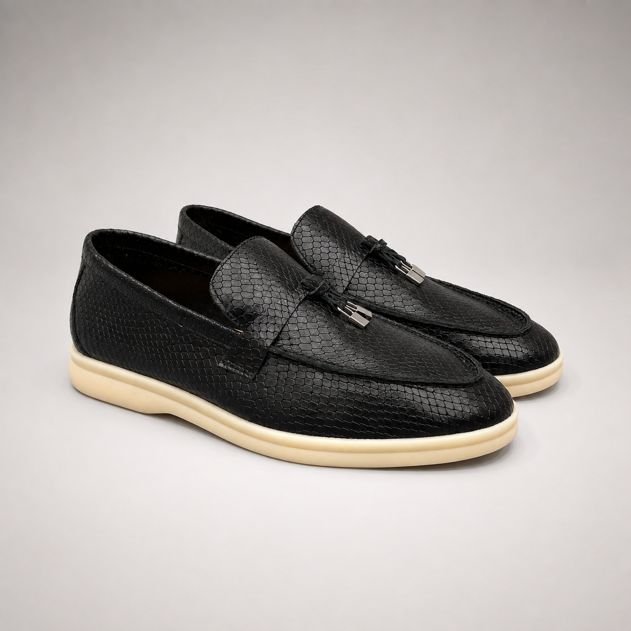 Black loafer pair three-quarter view showing a snakeskin-pattern embossed vamp and tassel detail