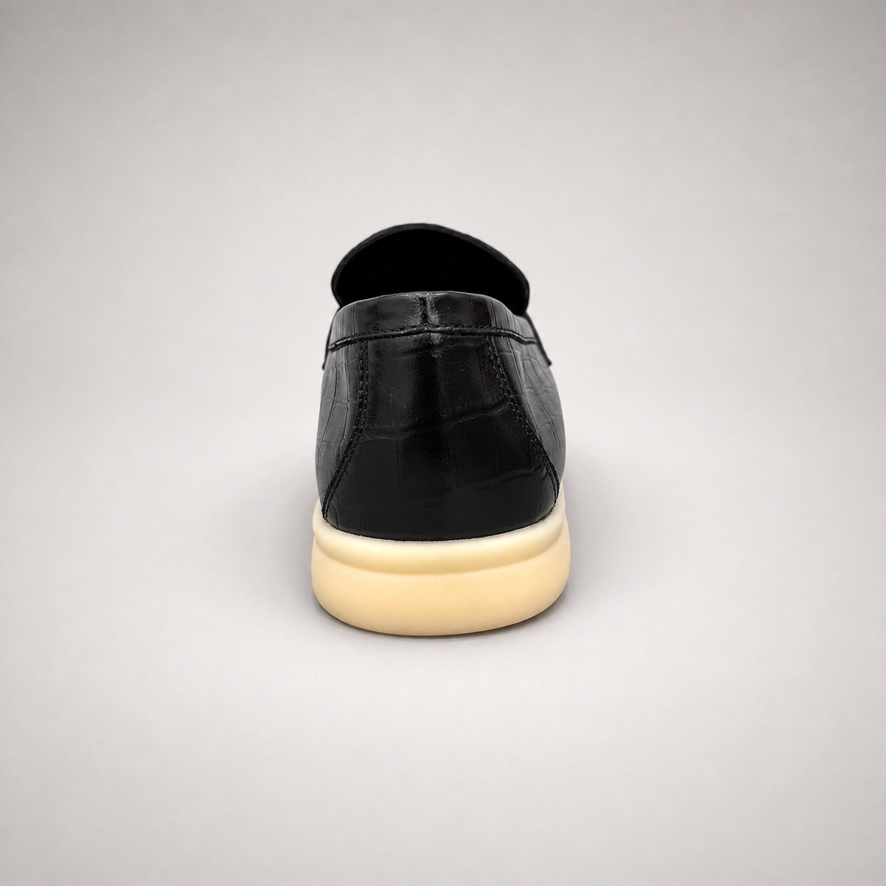 Black loafer rear view showing a crocodile-pattern embossed upper and metal accent