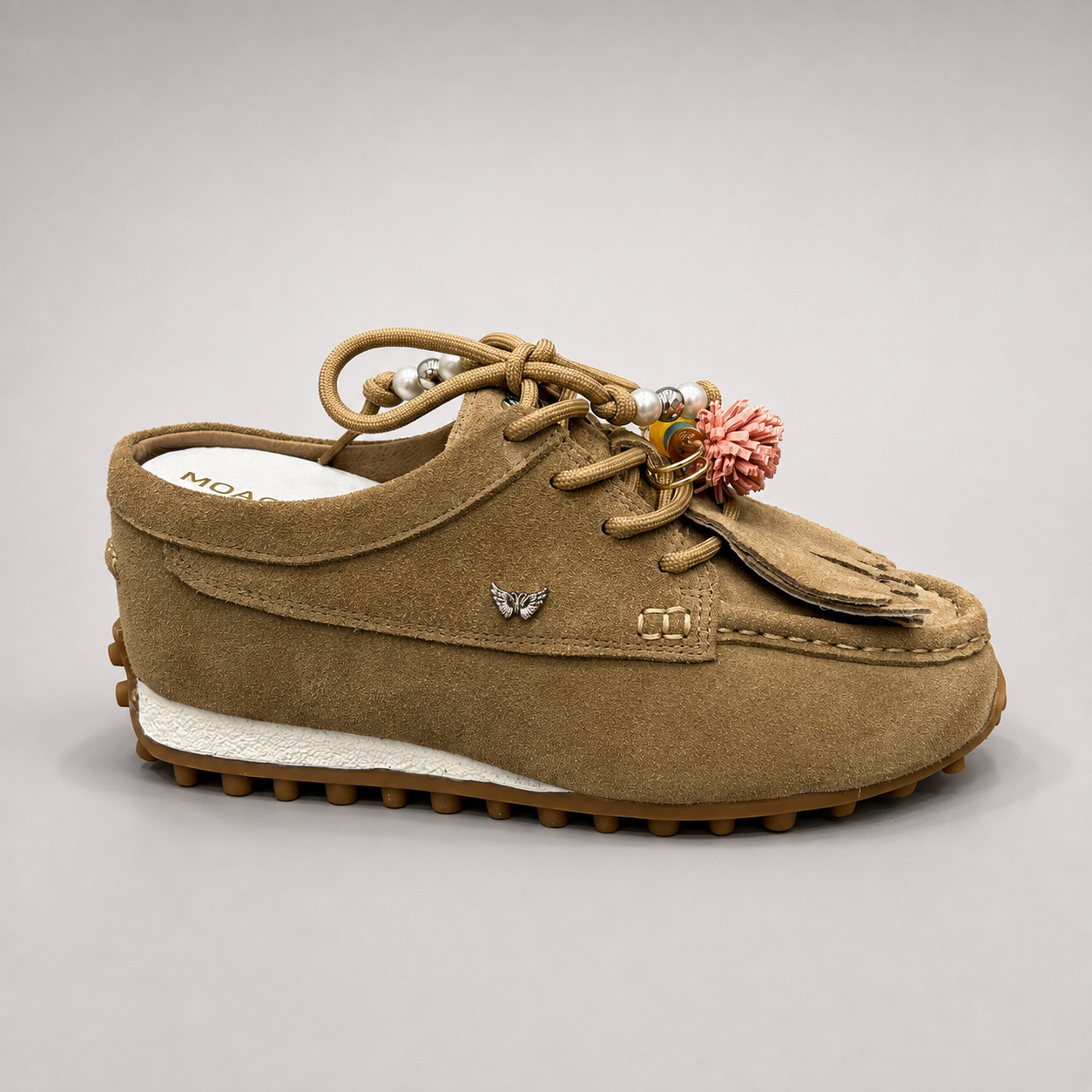 Tan moccasin sneaker side profile showing fringe and tassel details over the laces