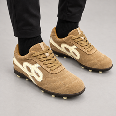 Beige suede studded lace-up soccer shoes worn with navy athletic trousers and white socks