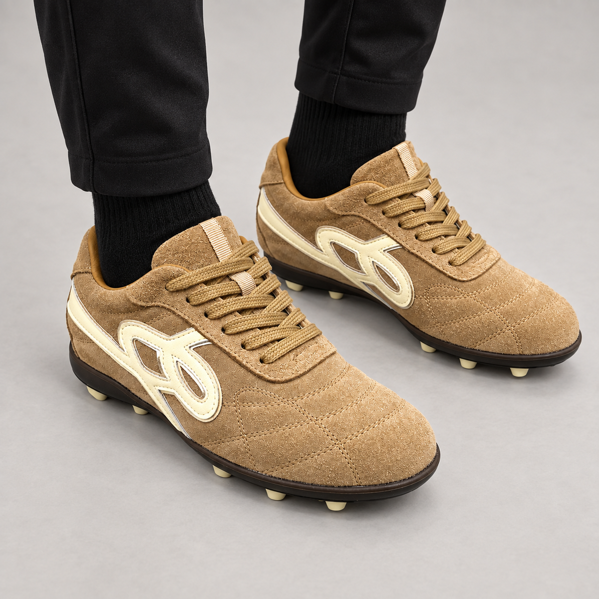 Beige suede studded lace-up soccer shoes worn with navy athletic trousers and white socks