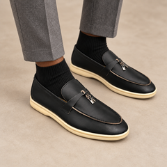 Black waxed leather metal-accent loafers worn with gray trousers and black socks