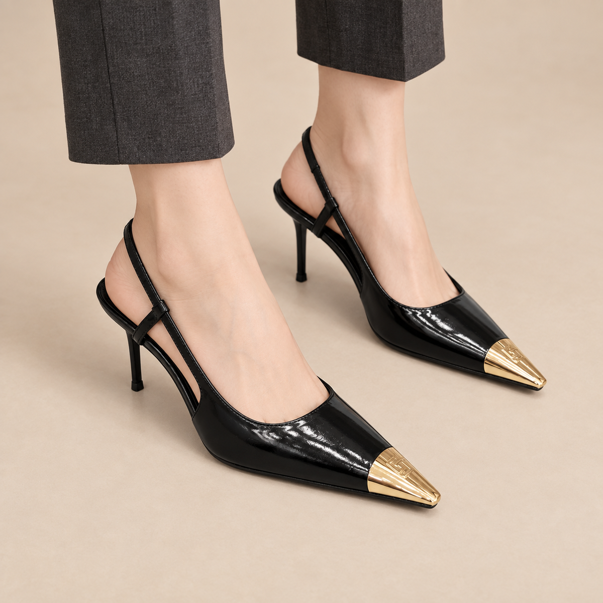 Black patent pointed-toe sculpted-heel slingback pumps worn with sand trousers