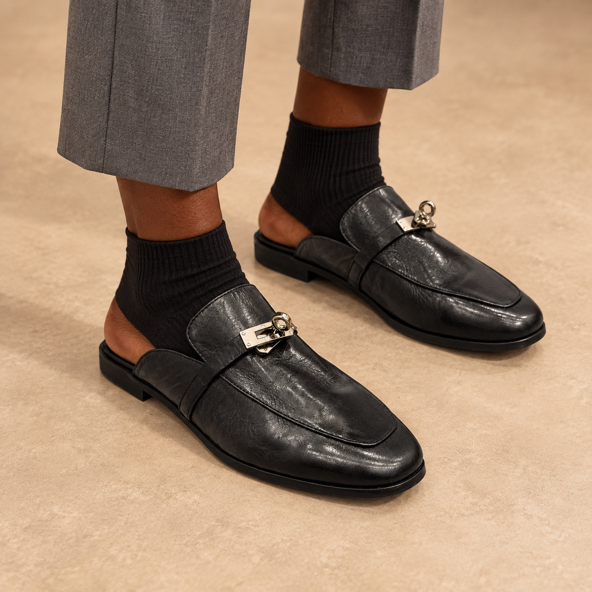 Black washed horse leather metal-accent mule loafers worn with gray trousers and black socks