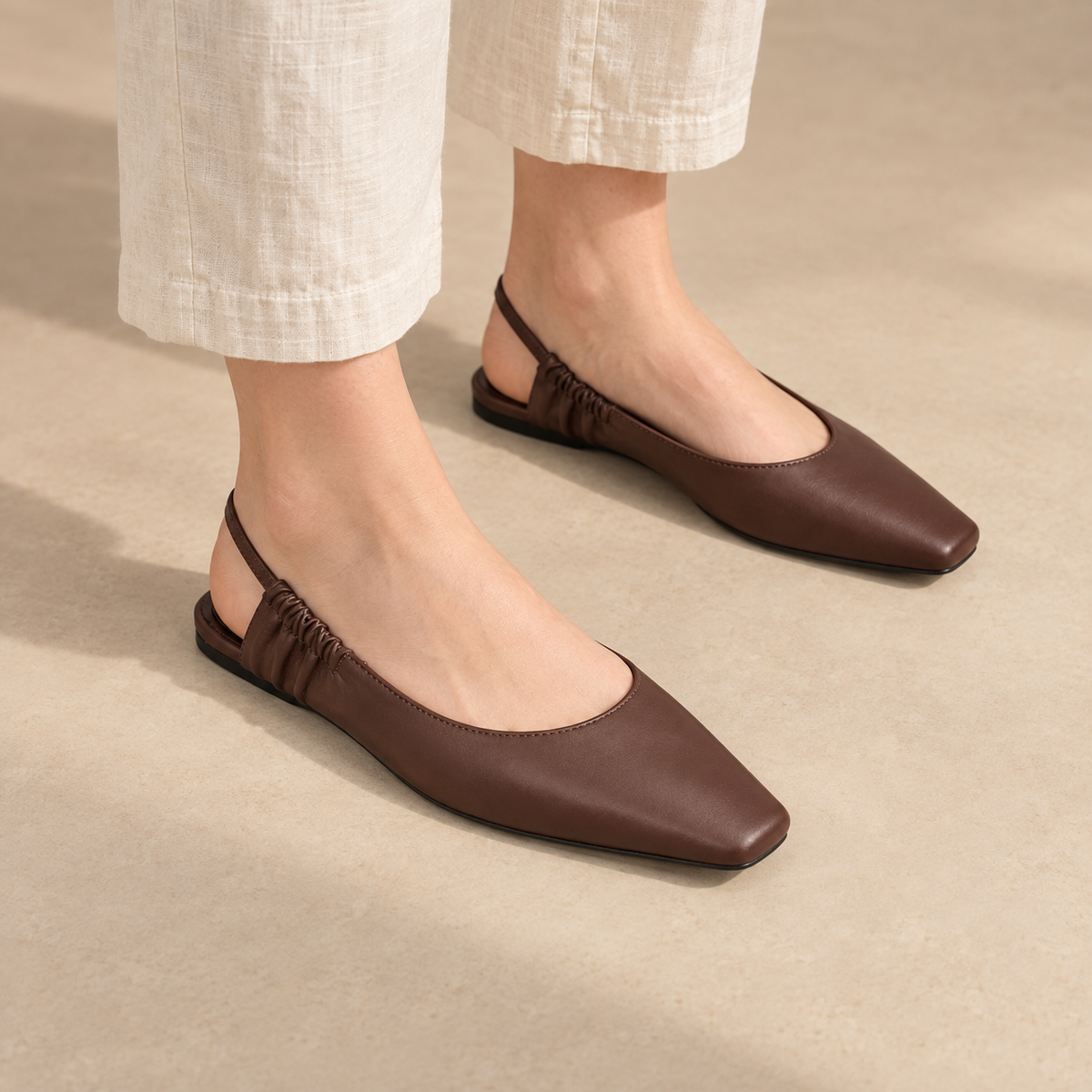 Brown square-toe gathered-strap slingback flats worn with cream linen trousers