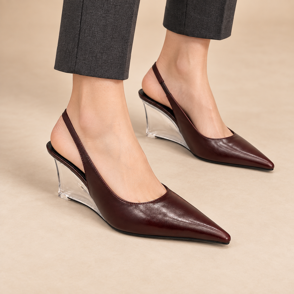 Burgundy pointed-toe clear-wedge slingback pumps worn with charcoal trousers