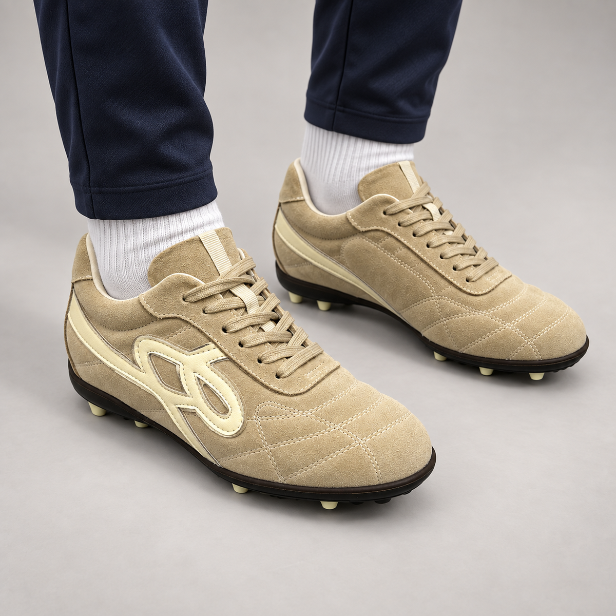 Tan suede studded lace-up soccer shoes worn with black athletic trousers and black socks
