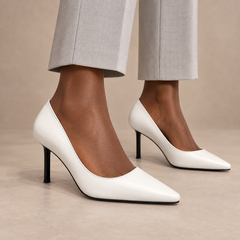 White pointed-toe leather pumps worn with pale gray trousers